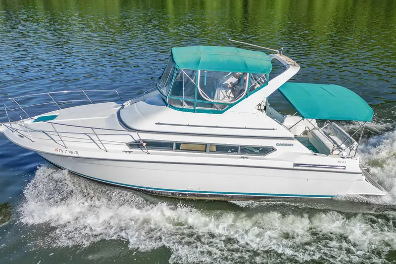 Slide: The Image of 1994 Carver 380 Santego yacht cruising on a serene lake with teal canopy. - 6