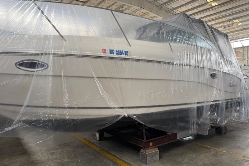 The Image of 2002 Rinker Fiesta Vee 310 boat covered in plastic wrap, stored indoors. - 1