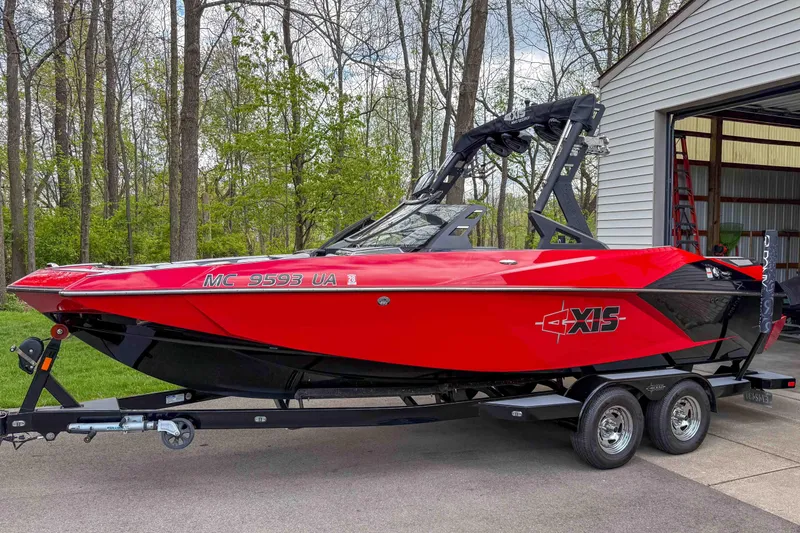 The Image of Red 2016 Axis A22 boat on trailer, parked near a garage in a wooded area. - 1