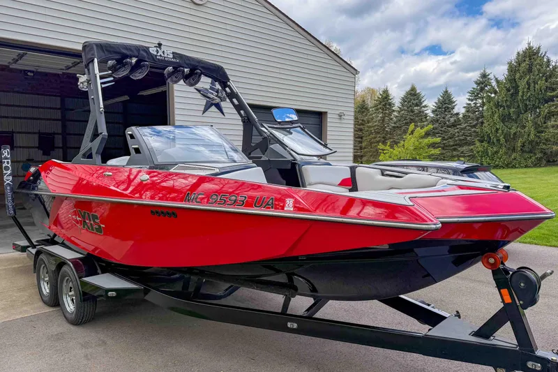 Slide: The Image of Red 2016 Axis A22 boat on trailer, parked near a garage with trees in the background. - 4