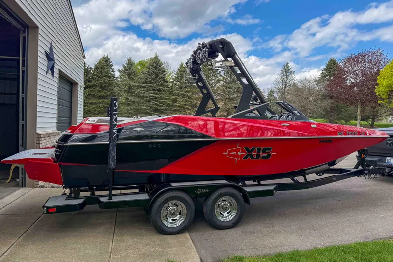 Slide: The Image of 2016 Axis A22 boat in red and black on a trailer, parked near a garage. - 6