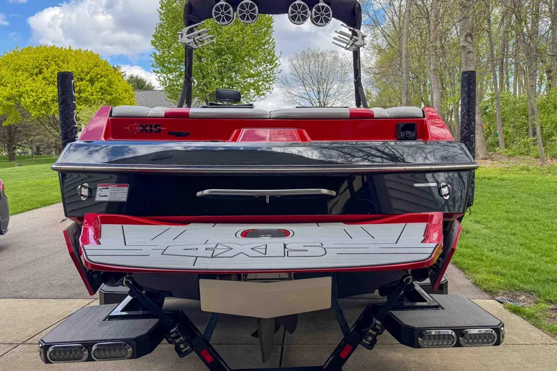 Slide: The Image of 2016 Axis A22 boat, rear view, red and black design, parked on driveway near trees. - 7