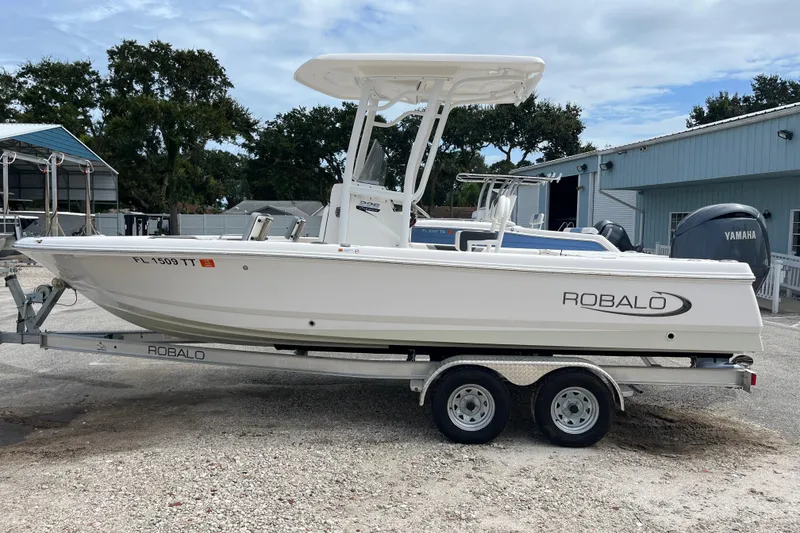 The Image of 2024 Robalo 226 Cayman boat on trailer, parked outdoors near a blue building. - 1