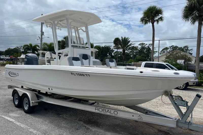 Slide: The Image of 2024 Robalo 226 Cayman boat on trailer, parked outdoors with palm trees in background. - 6
