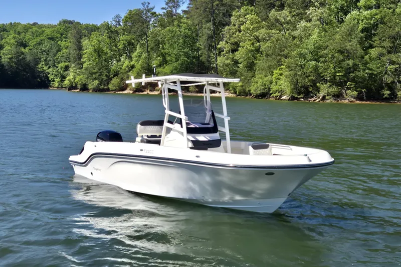 The Image of 2023 Bayliner Trophy T22CC boat cruising on a scenic lake with lush green trees. - 1