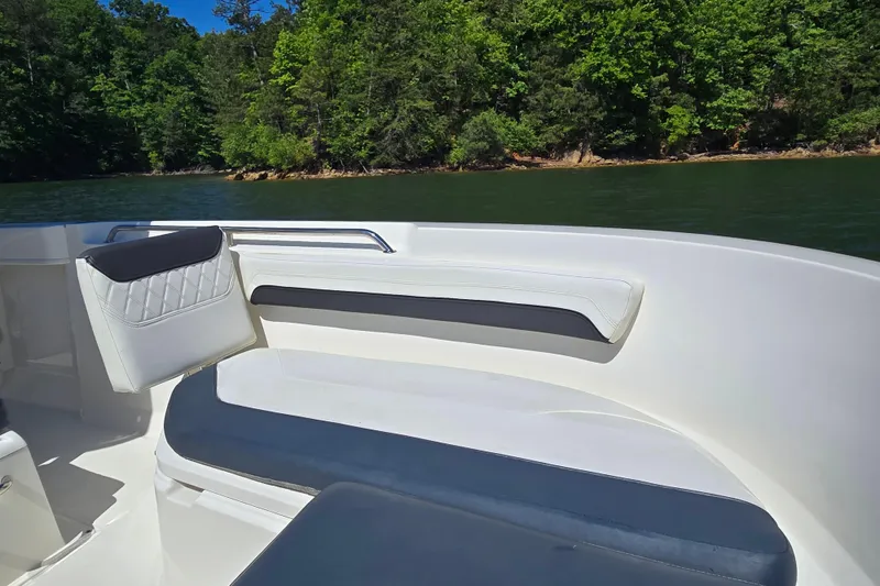 Slide: The Image of 2023 Bayliner Trophy T22CC boat interior with cushioned seating, near lush green shoreline. - 12
