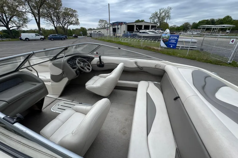 Slide: The Image of 2000 Crownline 180 BR boat interior with white seating and steering wheel, parked outdoors. - 5