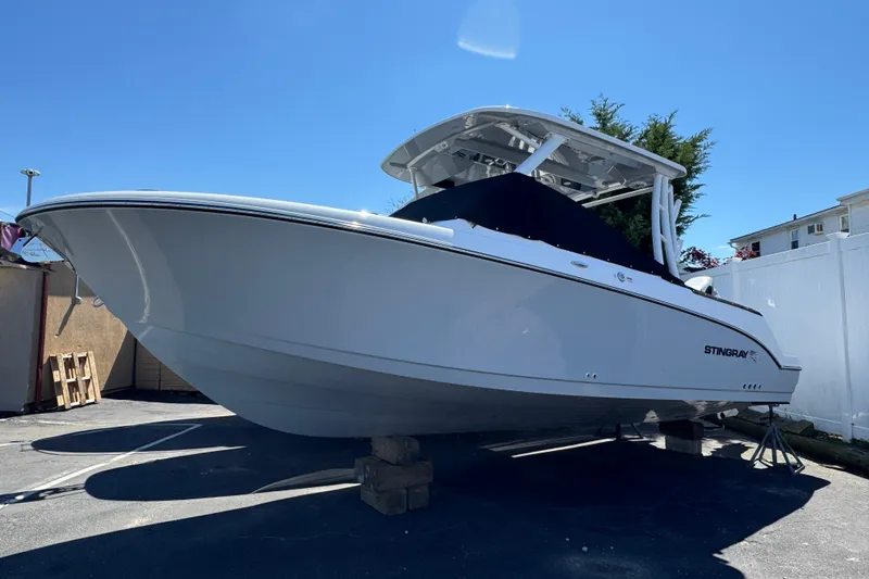 The Image of 2026 Stingray 259 DC boat on display, white hull, parked outdoors under clear blue sky. - 1