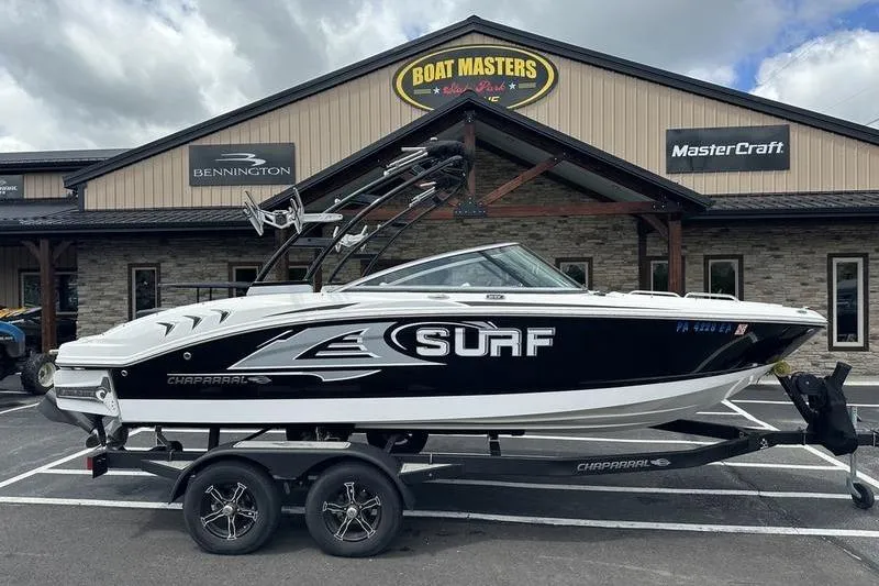The Image of 2021 Chaparral 21 Surf boat on trailer outside dealership, featuring sleek black and white design. - 1