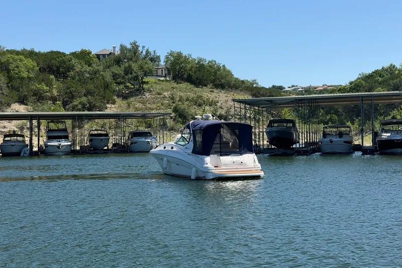 Slide: The Image of 2006 Sea Ray Sundancer 320 cruising near a marina with docked boats and lush greenery. - 18