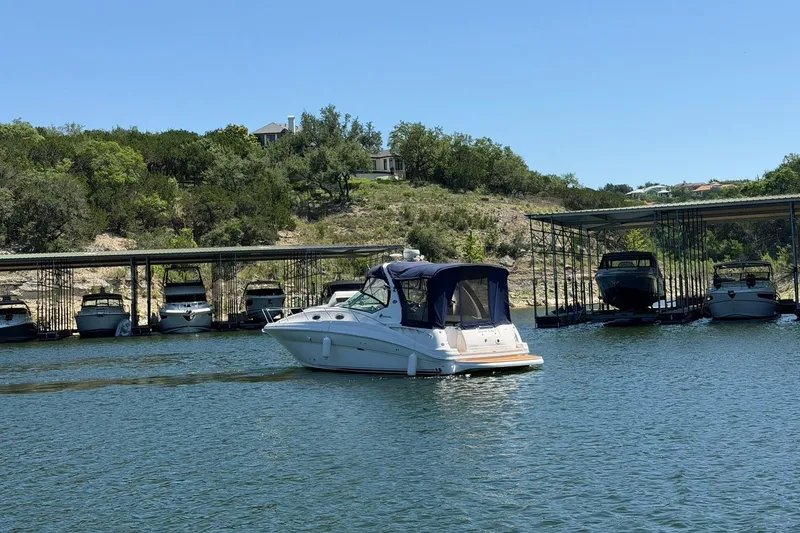 Slide: The Image of 2006 Sea Ray Sundancer 320 cruising near a marina with docked boats and lush greenery. - 19