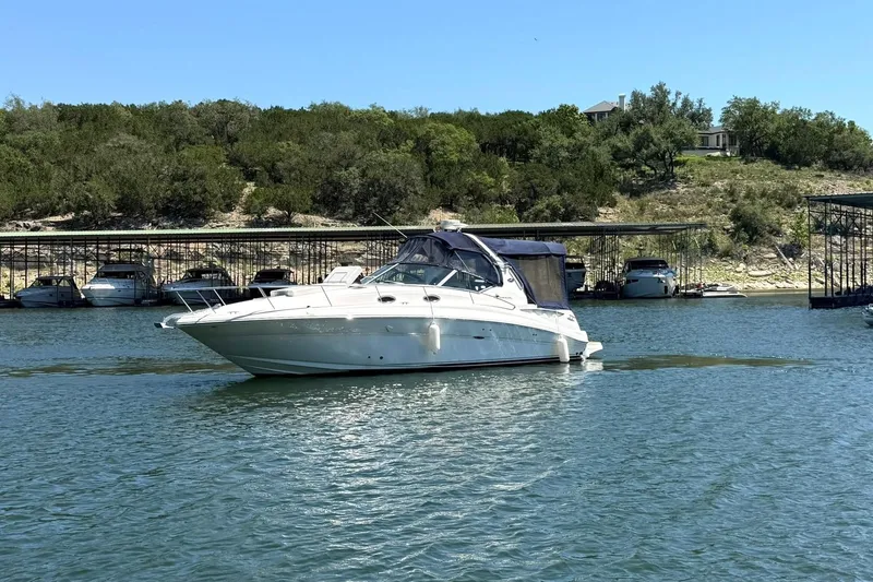 Slide: The Image of 2006 Sea Ray Sundancer 320 yacht on a serene lake with docked boats in the background. - 7