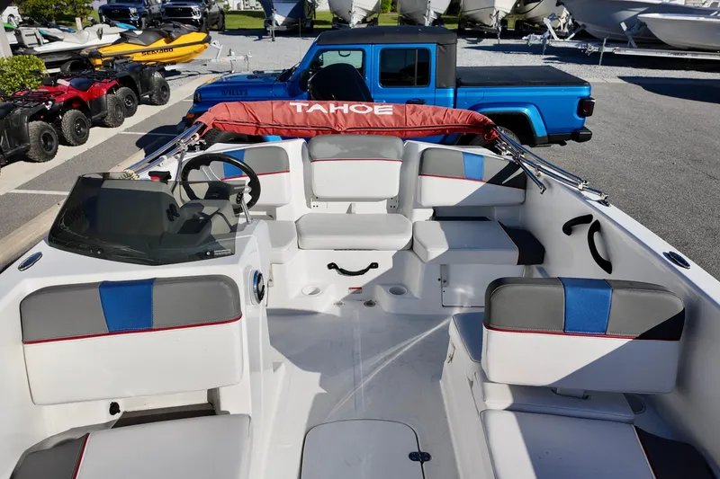 Slide: The Image of 2024 Tahoe T18 boat interior with seating, steering wheel, and dashboard, parked near vehicles. - 2