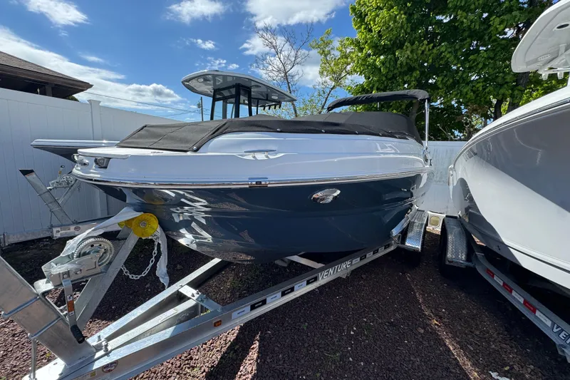The Image of 2026 Stingray 211 DC boat on trailer, parked outdoors under a clear blue sky. - 1