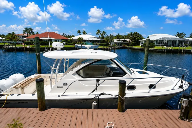 Slide: The Image of 2016 Pursuit OS 325 Offshore boat docked by waterfront homes under blue sky. - 2