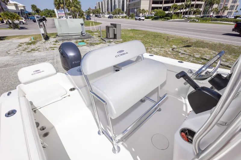 Slide: The Image of 2014 Cobia 214 Center Console boat interior with seating and controls, parked near a road. - 40