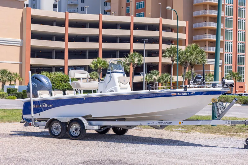 The Image of 2015 NauticStar 214 XTS boat on trailer, parked near modern buildings and palm trees. - 0