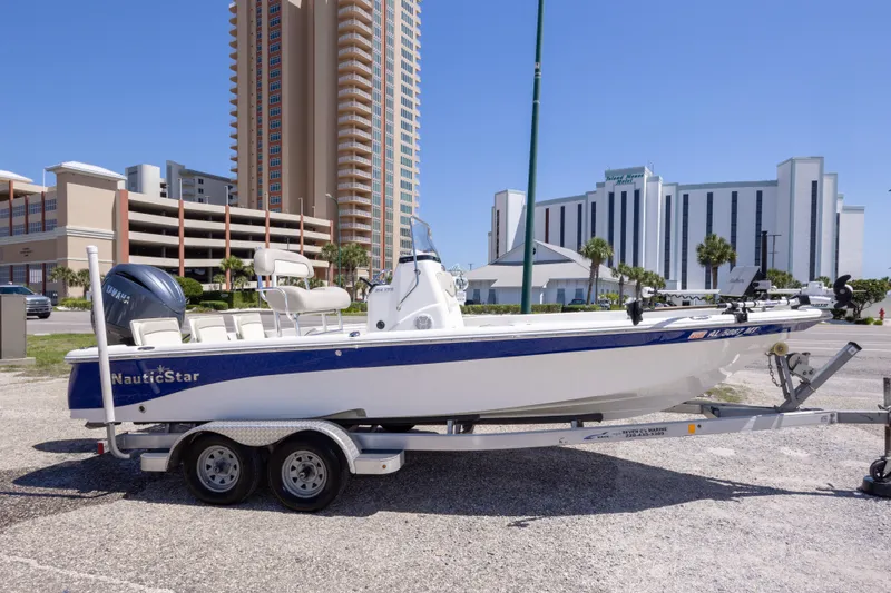 Slide: The Image of 2015 NauticStar 214 XTS boat on trailer, parked near tall buildings under clear blue sky. - 10