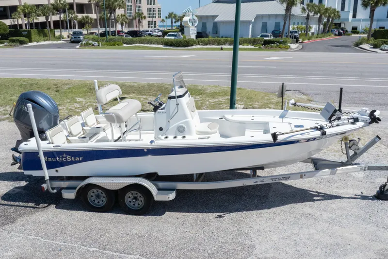 Slide: The Image of 2015 NauticStar 214 XTS boat on trailer, parked near a road with buildings in background. - 12