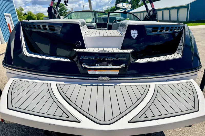 Slide: The Image of 2014 Nautique Super Air Nautique 210 boat rear view with sleek design and logo. - 16