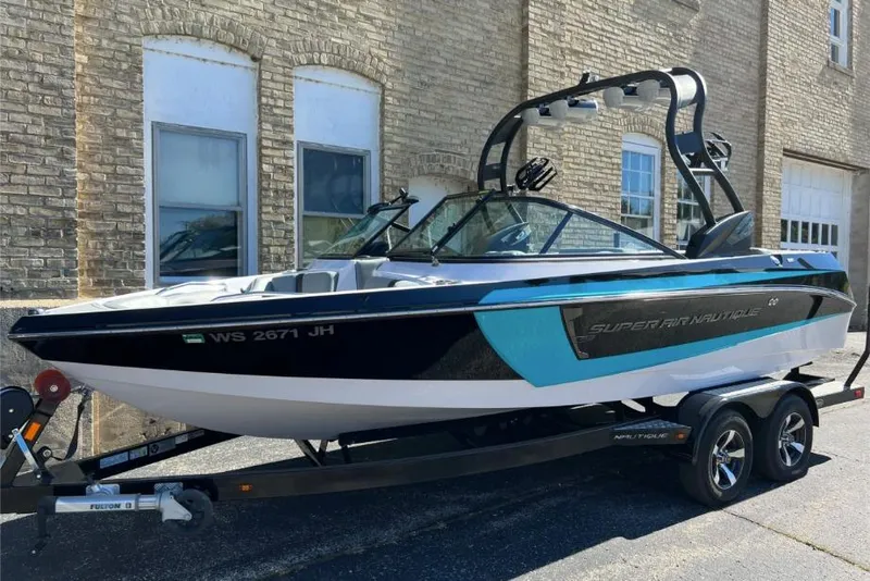 Slide: The Image of 2014 Nautique Super Air Nautique 210 boat on trailer, parked by brick building. - 3