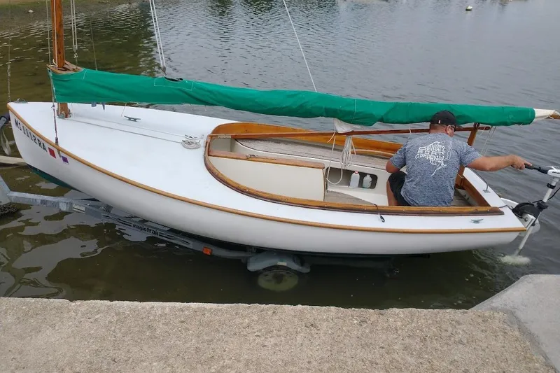 Slide: The Image of 1997 COMPASS CLASSIC Catboat with green sail cover, docked on a trailer by the water. - 4
