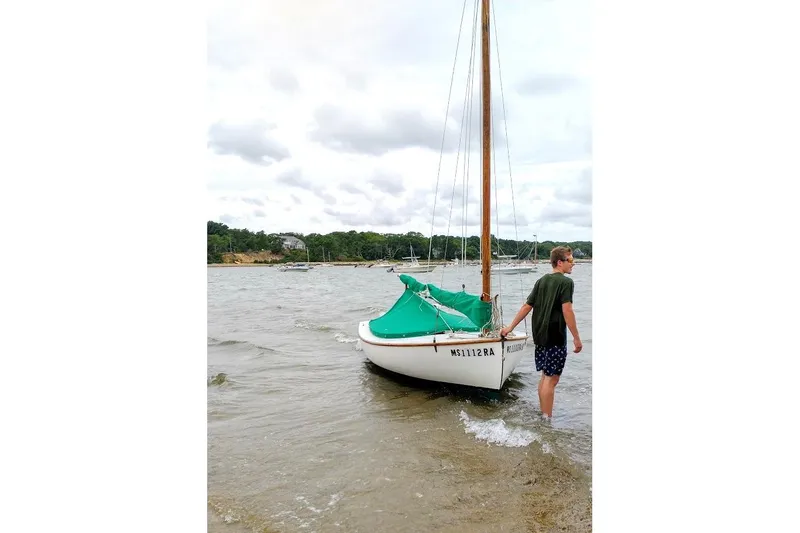 Slide: The Image of A person stands beside a 1997 COMPASS CLASSIC Catboat on a calm shoreline. - 5