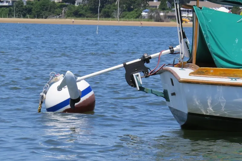 Slide: The Image of 1997 COMPASS CLASSIC Catboat moored on calm water with buoy and green cover. - 6