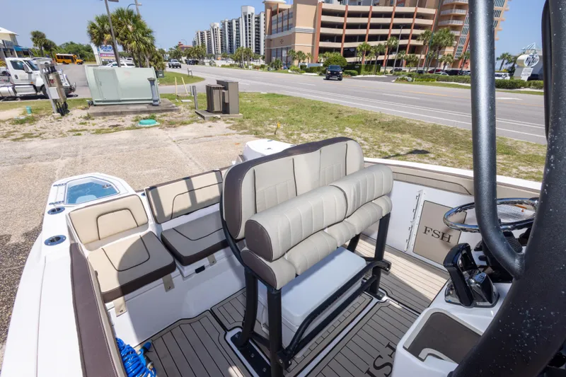 Slide: The Image of 2025 Yamaha Boats 255 FSH Sport E interior with seating and helm, parked near a road. - 44