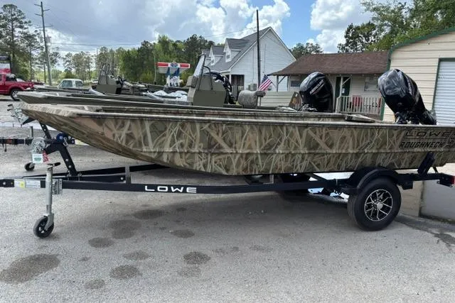The Image of 2026 Lowe Roughneck 1660 Deluxe Tiller boat on trailer, camo design, parked outdoors. - 1