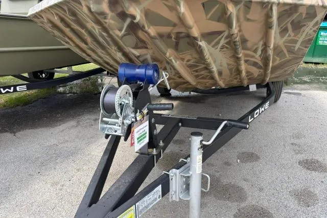 Slide: The Image of 2026 Lowe Roughneck 1660 Deluxe Tiller boat on trailer, featuring camouflage design and winch system. - 4