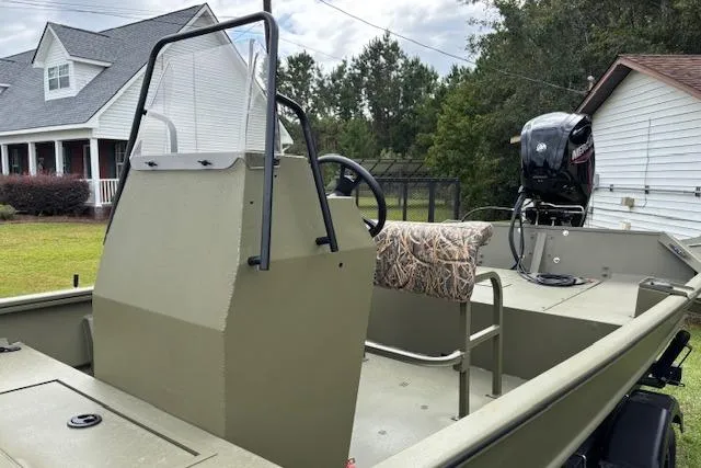 Slide: The Image of 2026 Lowe Roughneck 1760 Deluxe Tiller boat with camouflage seating, parked near houses. - 2