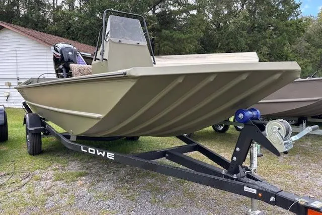 Slide: The Image of 2026 Lowe Roughneck 1760 Deluxe Tiller boat on trailer, parked outdoors. - 3