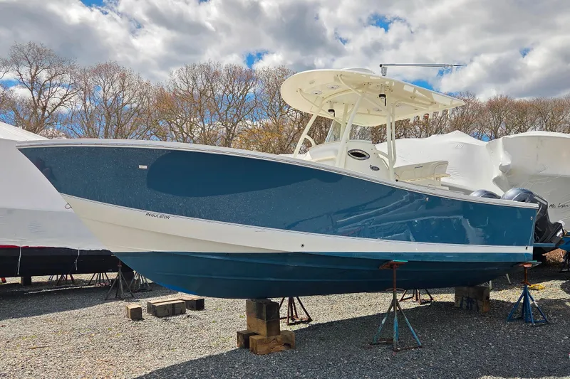 The Image of 2014 Regulator 25 boat on stands, blue hull, outdoor storage. - 0