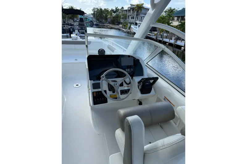 Slide: The Image of 2023 World Cat 255 DC boat helm with steering wheel and controls, docked by waterfront homes. - 7