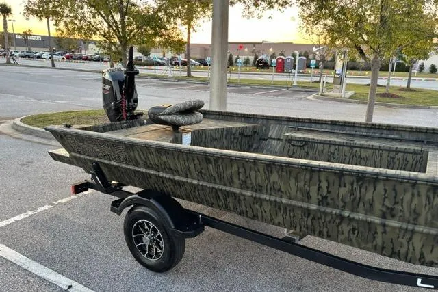 Slide: The Image of 2026 Lowe Roughneck 1760 Deluxe Tiller boat on trailer in parking lot at sunset. - 2