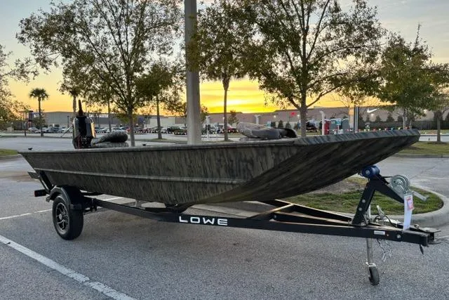 Slide: The Image of 2026 Lowe Roughneck 1760 Deluxe Tiller boat on trailer at sunset in parking lot. - 3