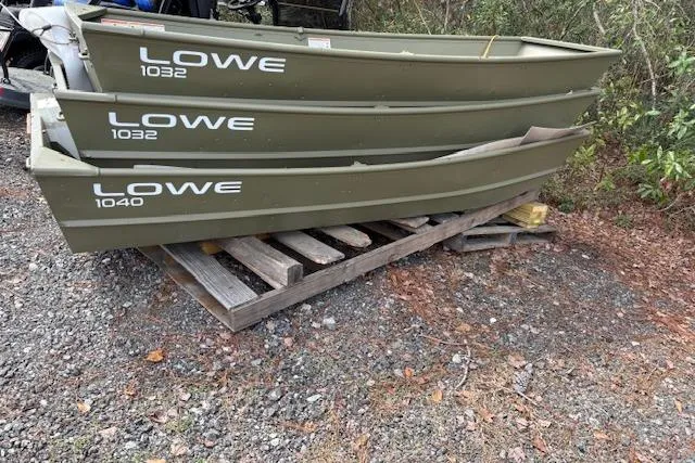 The Image of Stacked Lowe Jon boats, models 1032 and 1040, on wooden pallets outdoors. - 1
