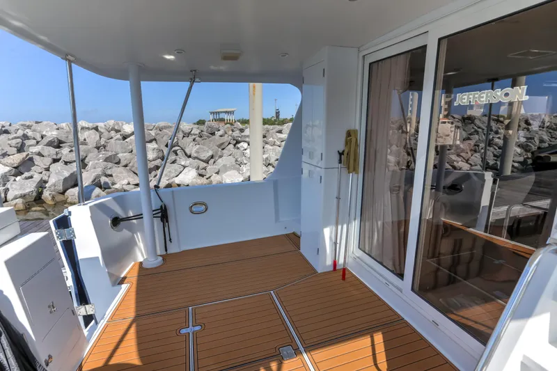 Slide: The Image of 2003 Jefferson Pilothouse 57 yacht deck with wooden flooring and glass doors, docked by rocky shore. - 16