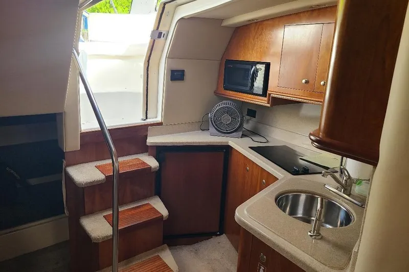 Slide: The Image of 2006 Cruisers Yachts 3470 Express interior kitchen with sink, microwave, and wooden cabinetry. - 4