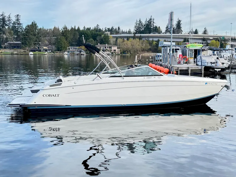 Slide: The Image of 2023 Cobalt R8 boat docked on a calm lake with trees and buildings in the background. - 22