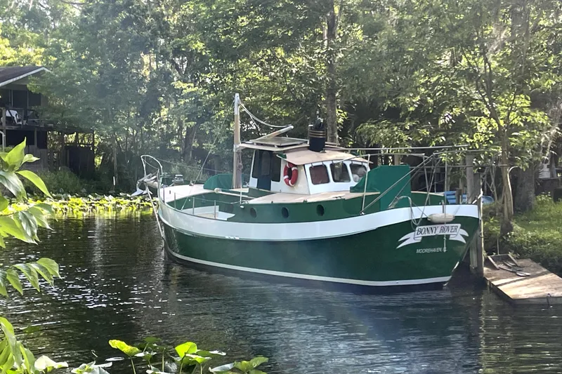 Slide: The Image of Green and white 1995 Bonny Rover boat docked in a lush, wooded area. - 2