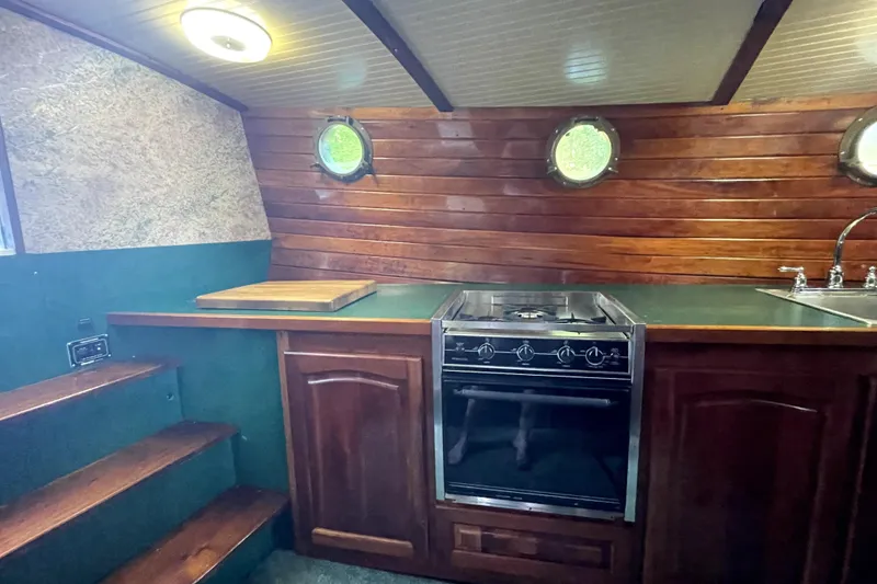 Slide: The Image of Cozy 1995 Bonny Rover boat kitchen with wooden cabinetry, stove, and porthole windows. - 22