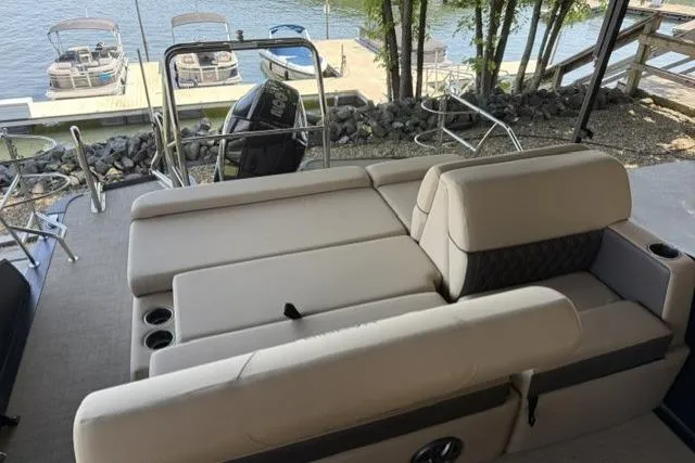 Slide: The Image of 2025 Harris Sunliner 230 boat with beige seating, docked by a serene lakeside. - 15
