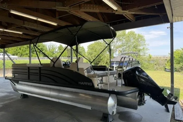 Slide: The Image of 2025 Harris Sunliner 230 pontoon boat under shelter, featuring sleek design and modern amenities. - 2