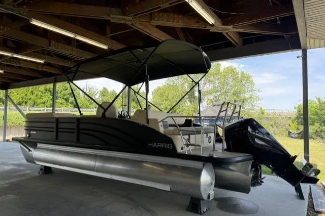 Slide: The Image of 2025 Harris Sunliner 230 pontoon boat under a wooden shelter, featuring a sleek black design. - 3