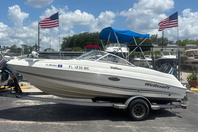 The Image of 2002 Wellcraft 180 Sportsman boat on trailer, American flags in background, sunny day. - 1