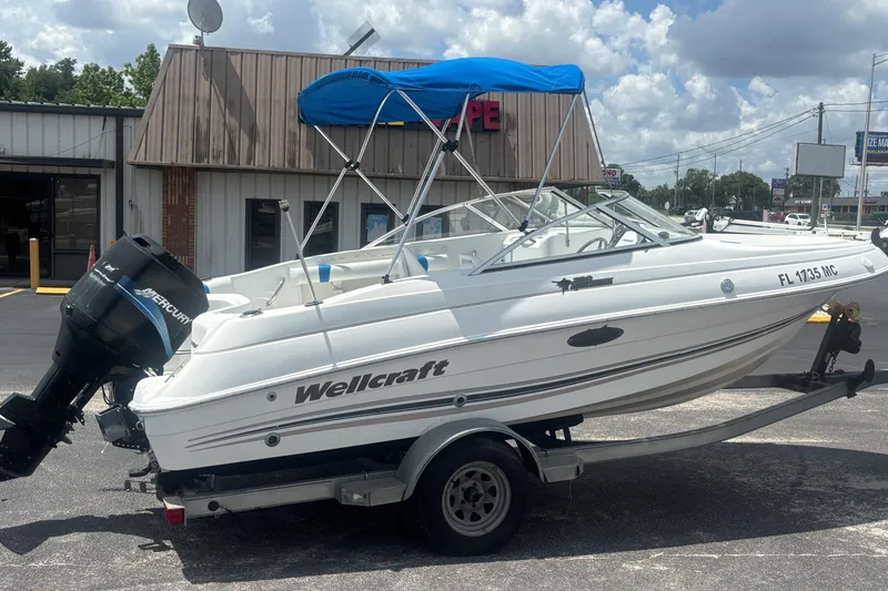 Slide: The Image of 2002 Wellcraft 180 Sportsman boat on trailer with blue canopy, parked outside a building. - 5