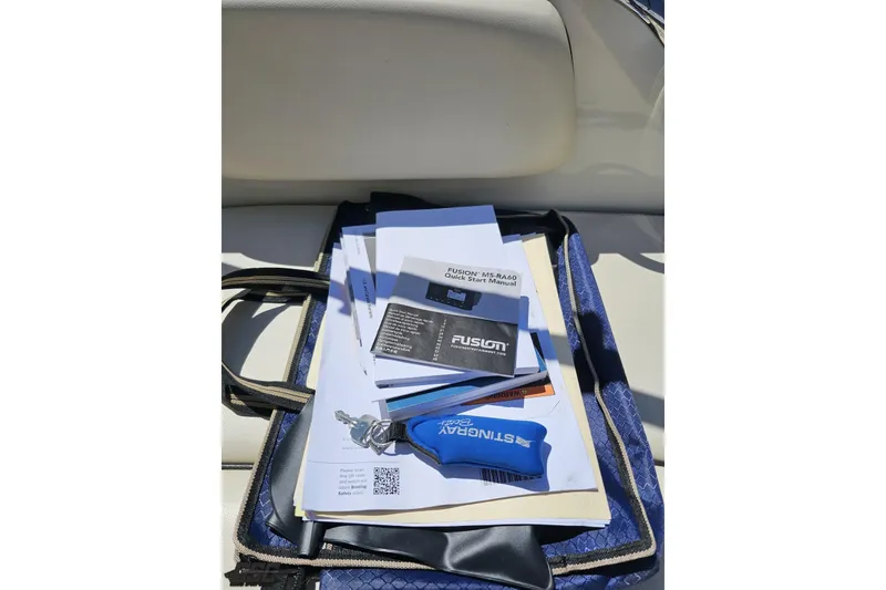 Slide: The Image of 2023 Stingray 182 SC boat manuals and accessories on seat, featuring Fusion MS-RA60 guide. - 45