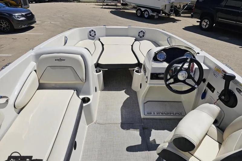 Slide: The Image of 2023 Stingray 182 SC boat interior with seating, steering wheel, and controls in a parking lot. - 48